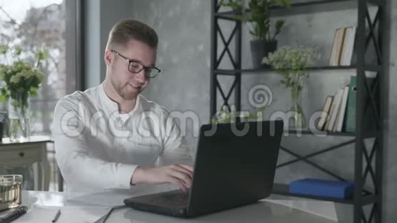 从事计算机工作的年轻男性企业家在网上开展业务工作完成询问和坐在桌上感到快乐视频的预览图