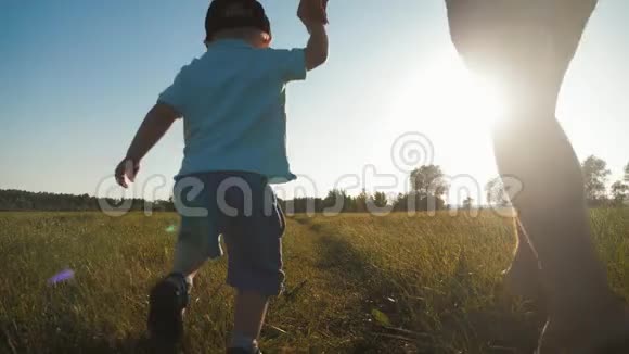 快乐的男人和男孩在阳光明媚的草地上奔跑爸爸和他的孩子在田野间散步幸福家庭的概念视频的预览图