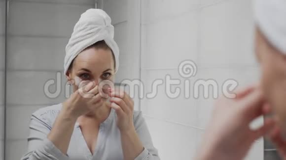 成年女性头上有一条毛巾她会去除眼睛下面的胶原蛋白垫然后照镜子视频的预览图