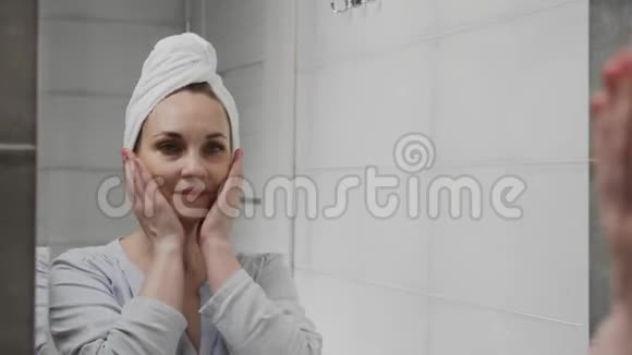 一个白人女人头上拿着毛巾在浴室的镜子前洗脸护肤健康视频的预览图