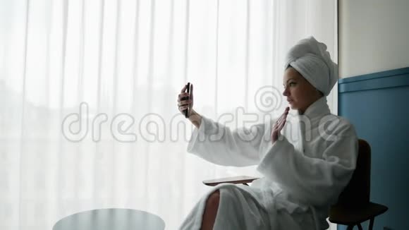 美丽的女博主穿着浴袍头上戴着毛巾在手机上拍摄现场视频视频的预览图