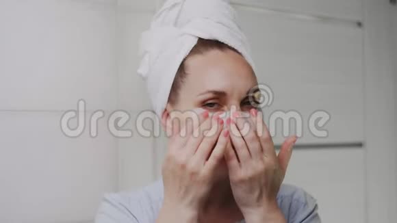 一位头上戴着毛巾的成年女性特写镜头移除了她眼睛下面的胶原蛋白垫并看着镜头视频的预览图