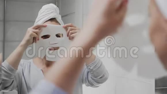 头上戴着毛巾的成年女性在脸上敷上口罩看着镜头视频的预览图