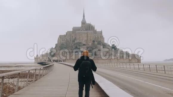 镜头跟随快乐兴奋的旅游者背着背包在诺曼底慢步走向史诗般的圣米歇尔山城堡视频的预览图