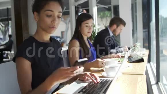 女商人在咖啡店用手提电脑和手机视频的预览图