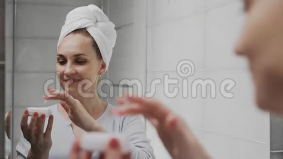 成年妇女头上戴毛巾涂奶油照镜子享受自然的美丽和健康视频的预览图