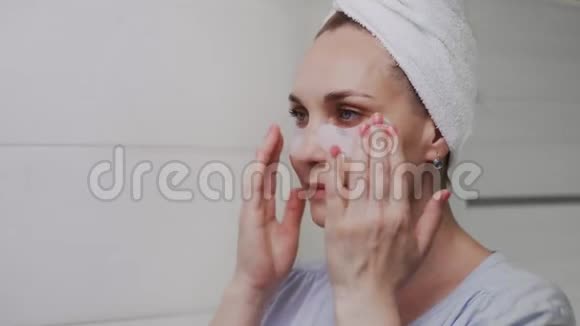 一位头上戴着毛巾的成年女性闭上双眼取下眼睛下面的胶原蛋白垫照镜子视频的预览图