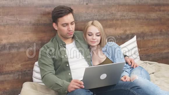 一对年轻的欧洲夫妇躺在卧室的床上用笔记本电脑看恐怖电影视频的预览图