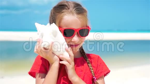 可爱的小女孩听着白色热带海滩上的一个大贝壳流动人口视频的预览图