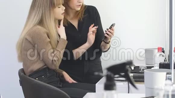 年轻女孩的客户拜访他的理发师在她的智能手机上选择新发型视频的预览图