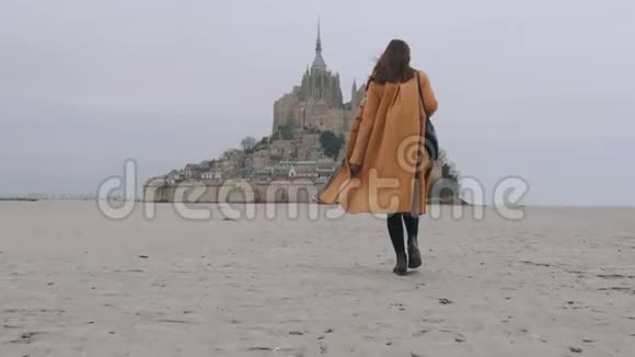 后景放大时尚旅游妇女慢慢走在海沙上史诗圣米歇尔城堡慢动作视频的预览图