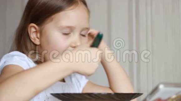 孩子用勺子吃汤在智能手机上看视频贴身女婴坐在家里做饭的桌子旁视频的预览图