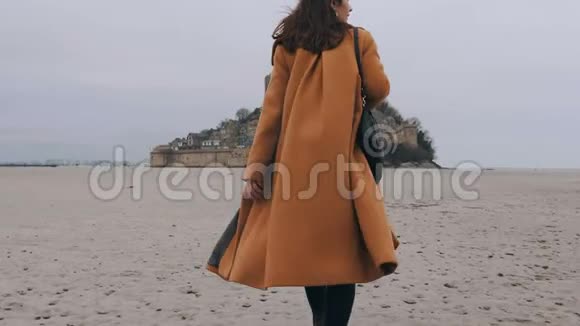 中型后景拍摄优雅快乐的博客女性走在海底沙滩在史诗圣米歇尔城堡慢动作视频的预览图