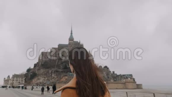 特写镜头跟随美丽的快乐女人走到史诗般的圣米歇尔山城堡在灰色阴天慢动作视频的预览图