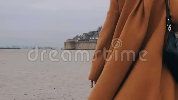 穿着优雅外套的贴身快乐旅游女人慢动作地朝诺曼底的圣米歇尔山城堡走去视频的预览图