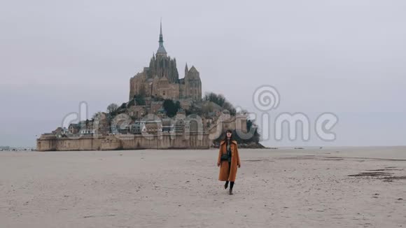在史诗圣米歇尔城堡慢跑中美丽的快乐旅游妇女在低潮海沙上慢慢行走视频的预览图
