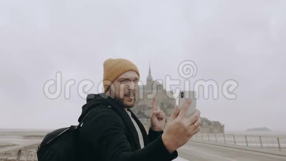 快乐年轻微笑的白种人博客男子使用智能手机在蒙特圣米歇尔城堡慢动作视频的预览图