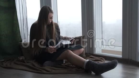 年轻漂亮的女孩在窗边看书视频的预览图