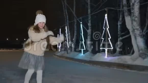 在冬季公园的冰场上跳舞的女孩在黑暗的夜晚滑冰快乐少女在冬冰上滑冰跳舞视频的预览图