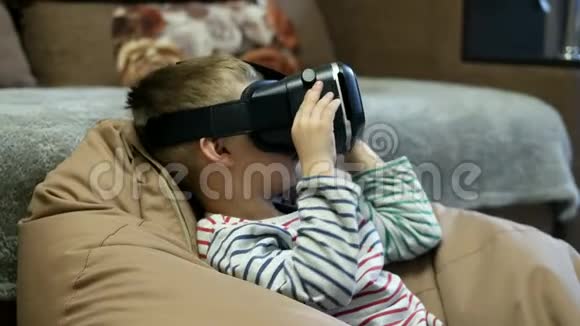 儿童戴虚拟现实眼镜在家里在软椅袋观看虚拟现实视频视频的预览图