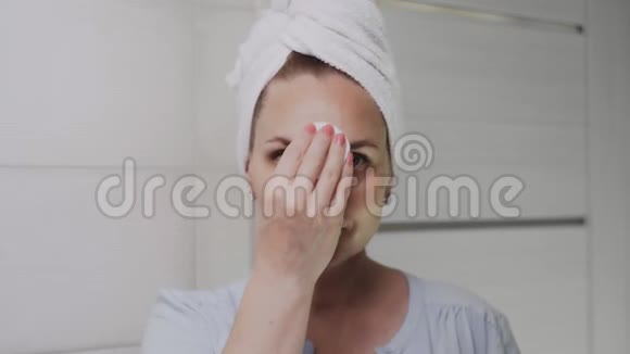 头上戴毛巾的成年女性涂上面霜看着镜头视频的预览图