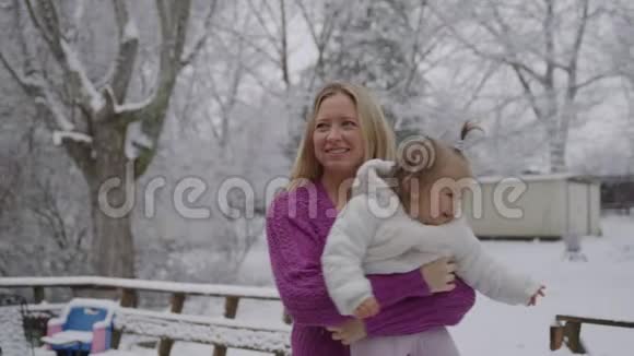年轻的金发女郎带着可爱的女婴在雪地公园里玩视频的预览图