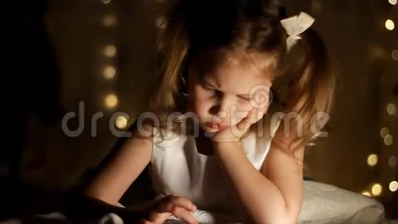 孩子躺在床上在黑暗的房间里玩智能手机女孩的近脸被一个视频的预览图