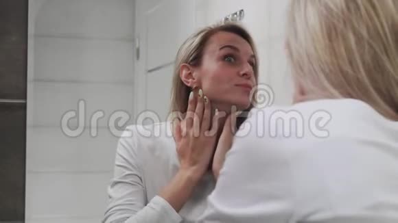 女人在眼睛下面涂上奶油照镜子享受自然的美丽和健康视频的预览图