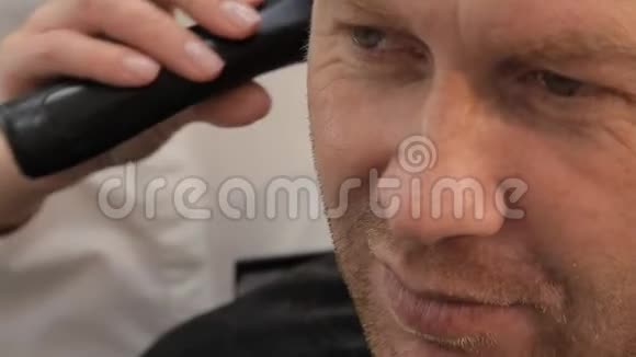 一个男理发师用无线修剪机和剪刀剪男人的眉毛快关门视频的预览图