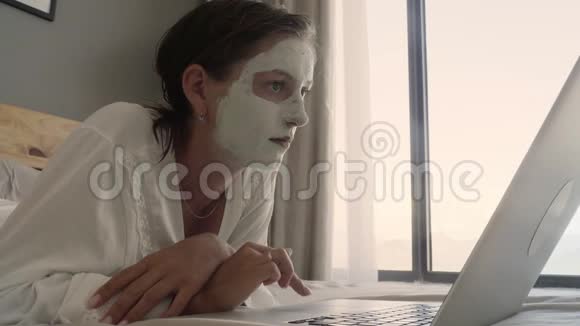 带化妆面具的女人床上有笔记本电脑视频的预览图