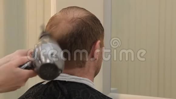 在理发店里为男人吹干头发一个女理发师给一个男人做头发在她的头发上吹暖风这个视频的预览图