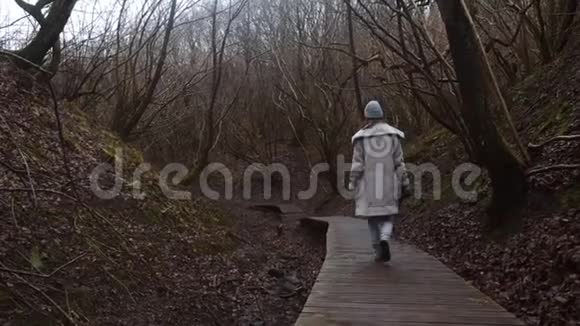 广角镜头中身穿白色冬衣的女子正带着相机沿着神秘的秋林小路慢悠悠地走着视频的预览图