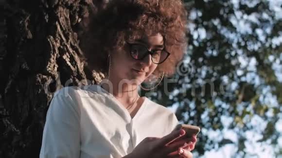 在公园里一个卷发女人正在用手机特写镜头视频的预览图