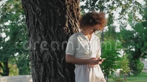 卷曲的女人在公共公园里使用手机视频的预览图