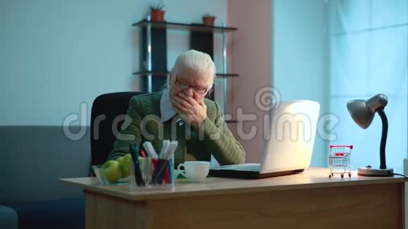 一位老年妇女咳嗽也许她病了坐在桌子旁在电脑旁工作视频的预览图
