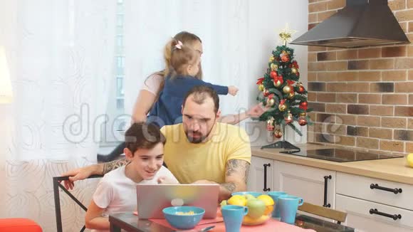 年轻漂亮的父母和孩子在厨房一起吃早餐时看电影或视频视频的预览图