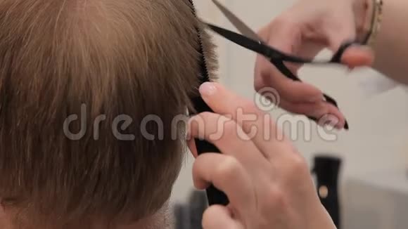 一个男人理发的特写一个理发师的女人用剪刀和梳子剪男人的头发视频的预览图