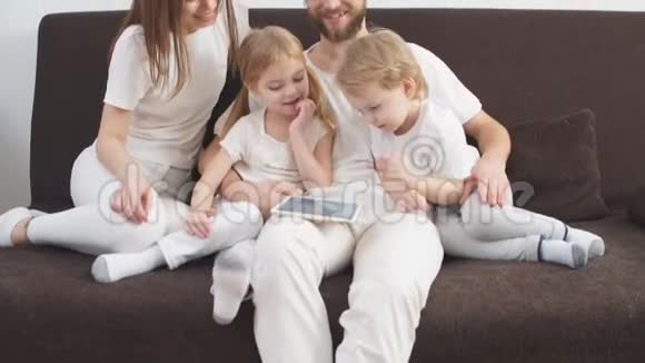 漂亮幸福一家人由母亲父亲儿子和女儿组成坐在家里的沙发上手里拿着平板电脑视频的预览图