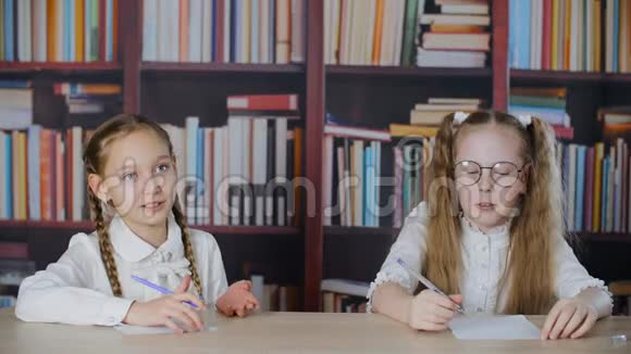 两个女孩在教室里的桌子上说话背景是书架快乐少年女孩同学聊天视频的预览图