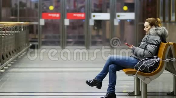 年轻漂亮的女士坐在宽敞明亮的大厅里的木凳上带着电话视频的预览图