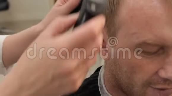 一个男人在理发店理发一位女理发师在客户的太阳穴和右耳理发这就是视频的预览图