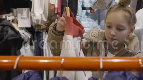 年轻的少女在购物时在服装陈列室里看夹克年轻女子在时装精品店挑选服装视频的预览图