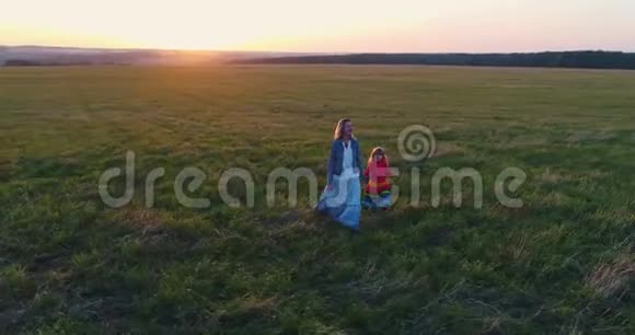 日落时分年轻的母亲和女儿一起在田野里散步空中观景视频的预览图