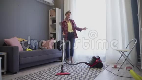 快乐的年轻女子在客厅里跳舞在家里用吸尘器清洁地毯视频的预览图