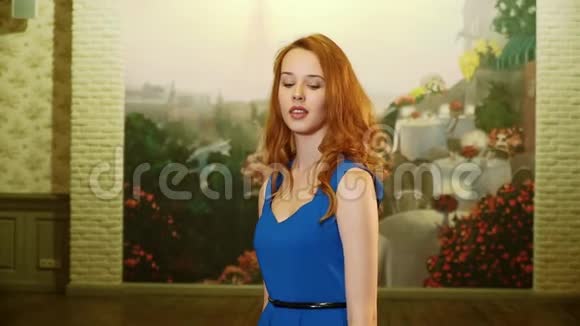 穿着蓝色连衣裙的漂亮性感女孩留着长长的红色头发和俏皮的样子旋转着微笑着看着镜头慢点视频的预览图