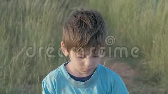 贫民窟的肖像小男孩地低着头站在田野上伤心的孩子在户外失去了家庭房子被摧毁了视频的预览图
