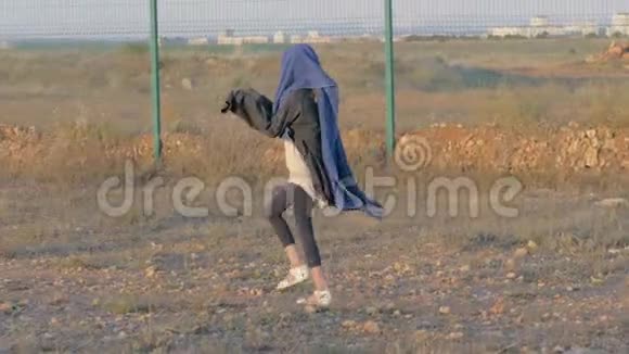 无家可归的儿童在保护区附近行走瘦小的难民女孩头上盖着被子沿着铁栅栏国家边界走概念视频的预览图