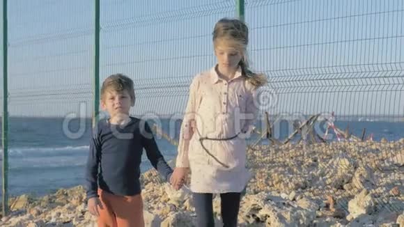 悲伤的难民儿童站在边境附近的海滩上限制区网围栏保护区悲伤的男孩和女孩站着视频的预览图