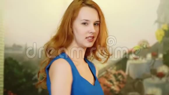 那个漂亮性感的女孩红头发穿着蓝色连衣裙看起来很俏皮她在旋转微笑着看着镜头懒汉视频的预览图