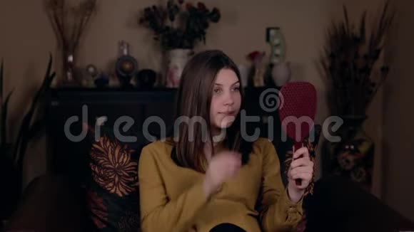 年轻漂亮的白人女子坐在扶手椅上直着头发照镜子视频的预览图